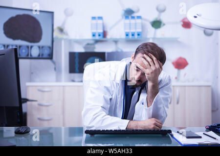 Müde junge Arzt versuchen, hielt seinen Kopf nach unten im Büro zu sitzen. Arzt im Labor. Stockfoto