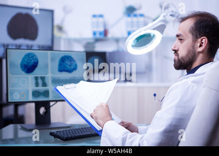 Portrait der junge Doktor seine Zwischenablage Noten Prüfung für seinen nächsten Chirurgie. Arzt suchen im Gehirn x-ray. Stockfoto