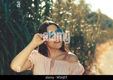 Porträt einer jungen Frau lächelnd und mit Sonnenbrille im Freien in einem/ Tag Stockfoto