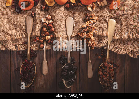 Getrocknete Früchte und Nüsse auf einen Löffel, Stoff und eine alte Tabelle angeordnet. Horizontale Zusammensetzung im alten Stil. Stockfoto