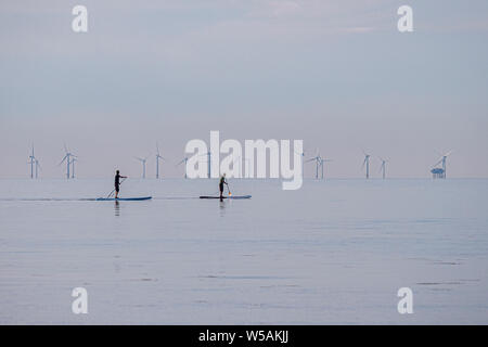 Paddlebarder auf einem Meer mit der Campion Wind Farm im Hintergrund - Worthing, West Sussex, Südengland, Großbritannien. Stockfoto