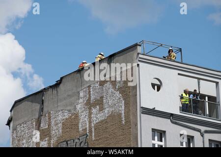 Berlin, Deutschland. 27. Juli, 2019. Feuerwehrmänner stehen auf dem Dach eines Mehrfamilienhauses in der Danziger Straße. Ein Feuer war in einem Apartment im Dachgeschoss des Gebäudes ausgebrochen. Quelle: Jörg Carstensen/dpa/Alamy leben Nachrichten Stockfoto