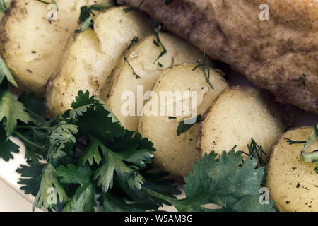 Auf dem Tisch auf einem Teller zwei Scheiben gebratenen Fisch, Bratkartoffeln, Dill, Petersilie. In enger vorgestellt. Stockfoto