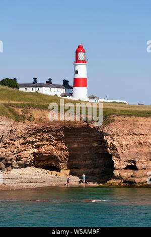 Der Strand und die Höhle in den Klippen am Byer's Loch/die Wherry mit Souter Leuchtturm oben. In der Nähe von Whitburn auf der South Tyneside Küste in Tyne und Wear Stockfoto