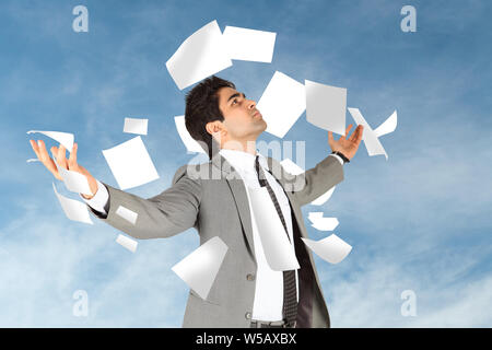 Papiere, die auf einen Geschäftsmann fallen, der mit ausgestreckten Armen steht Stockfoto