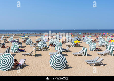 Sonnenanbeter in Sesseln entspannen Sie sich unter den Sonnenschirmen am Strand im Badeort an der belgischen Nordseeküste während der Hitzewelle im Sommer in Belgien Stockfoto