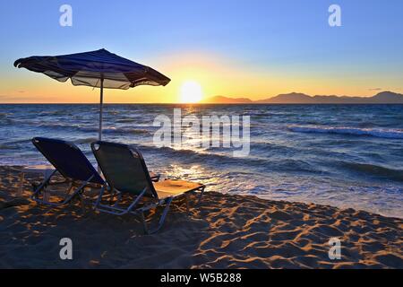 Sonnenliegen und Sonnenschirm am Strand bei Sonnenuntergang am Meer. Schöne Konzept für Urlaub, Ferien und Reisen. Stockfoto