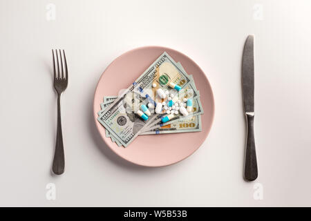 Pillen und Geld auf den Teller mit Messer und Gabel auf weißem Hintergrund Stockfoto