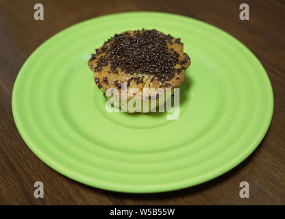 Vanilla Cupcake mit Chocolate Chips auf einem mint Farbe Untertasse. Eine Platte steht auf einem Holz- braun Tabelle Stockfoto