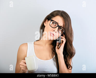 Unglücklich deprimiert schöne Frau Gespräch am Handy in Brillen und die Tasse Kaffee auf blauem Hintergrund mit der leere Raum. Closeup po Stockfoto