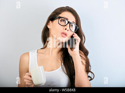 Unglücklich wütend schöne Frau Gespräch am Handy in Brillen und die Tasse Kaffee auf blauem Hintergrund mit der leere Raum. Nahaufnahme Stockfoto