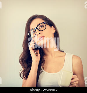 Ernsthafte schöne Frau Gespräch am Handy in Brillen und die Tasse Kaffee auf blauem Hintergrund mit der leere Raum. Closeup Vintage Port Stockfoto