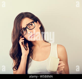 Unglücklich deprimiert schöne Frau Gespräch am Handy in Brillen und die Tasse Kaffee auf blauem Hintergrund mit der leere Raum. Closeup vi. Stockfoto