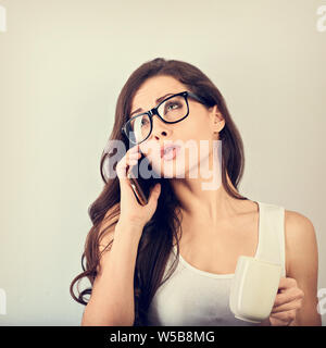 Unglücklich wütend schöne Frau Gespräch am Handy in Brillen und die Tasse Kaffee auf blauem Hintergrund mit der leere Raum. Closeup vintag Stockfoto