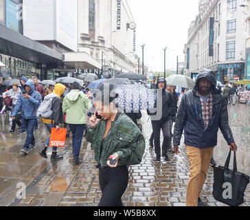 Manchester, Großbritannien. 27. Juli, 2019. Menschen laufen durch die Innenstadt von Manchester mit Sonnenschirmen bei starkem Regen. Credit: Yiannis Alexopoulos/SOPA Images/ZUMA Draht/Alamy leben Nachrichten Stockfoto