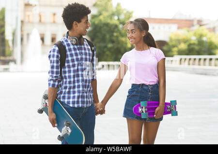 Teenage Paar mit skateboards halten sich an den Händen zu Fuß entlang der Straße der Stadt Stockfoto