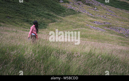 Junge unbekannte Frau zu Fuß auf der Wiese auf die Berge der Highlands von Schottland im Vereinigten Königreich Stockfoto
