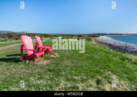 Zwei rote Adirondack Stühlen mit Blick auf den Ozean an der Küste von Neufundland im Gros Morne National Park, Kanada Stockfoto