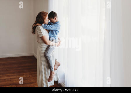 Seitenansicht der jungen Mutter Holding schulpflichtigen Sohn im Studio Stockfoto