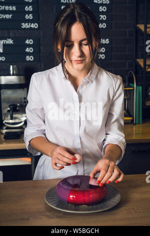 Junge schöne Frau in weißem Hemd dekorieren rosa Käsekuchen durch Fl Stockfoto