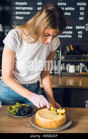 Junge und schöne Mädchen im weißen T-Shirt und rosa Handschuh dekorieren Kuchen Stockfoto