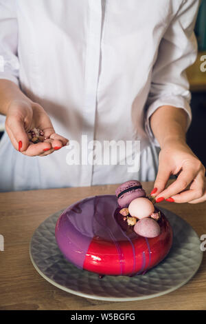 Frau Hände verzieren pink Cake von Makronen und Blumen. Nahaufnahme Stockfoto