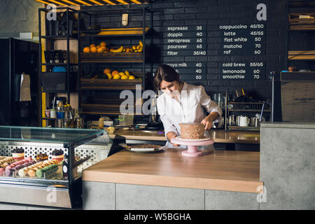 Frau in weißem Hemd schmücken Kuchen in einem Cafe vor Showcase Stockfoto