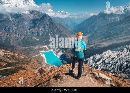 Stehende Frau mit Rucksack auf dem Berg. Schöne Berge in Wolken, See mit azurblauem Wasser bei Sonnenuntergang. Landschaft mit allein Mädchen, verschneite Ro Stockfoto