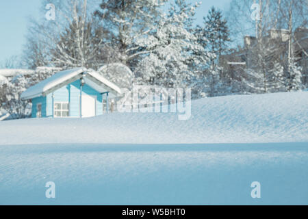 Winterlandschaft getönten in Blau. Antriebe des Schnees in der Sonne funkeln gegen einen unscharfen Hintergrund von einem kleinen Haus und Bäume mit Schnee bedeckt. Flach Stockfoto