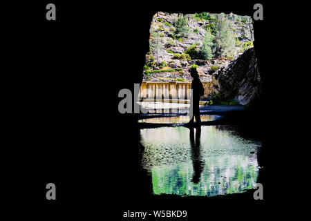 Mann vor der Ausfahrt zu einem Tunnel sitzen, Silhouette in einem flachen Teich widerspiegelt; Hetch Hetchy Reservoir, Yosemite National Park, Sierra Neva Stockfoto