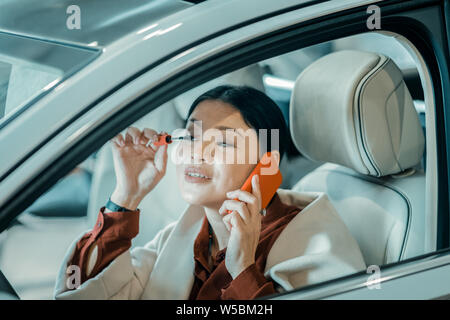 Beschäftigte Frau setzen auf maskara auf Fahrersitz. Stockfoto