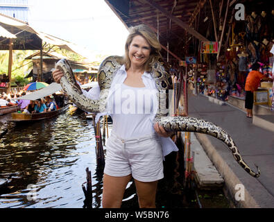 Eine glückliche Frau mittleren Alters touristische Holding eine Boa Constrictor Schlange in der Damneom Saduak Markt in der Nähe von Bangkok, Thailand, die eine große touristische Stockfoto