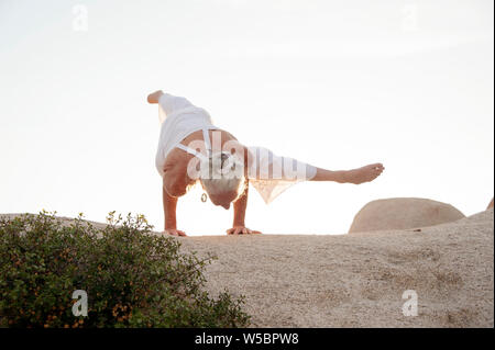 Seniro Frau in Yoga arm Balance auf Stein Landschaft. Stockfoto