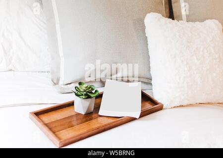 Nahaufnahme eines bequemen Bettes mit einem weißen Buch Neben einer kleinen Pflanze auf einem Holztablett Stockfoto