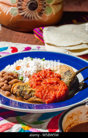 Mexikanische gefüllte Paprikas (Chiles Rellenos), poblano Chili mit Käse gefüllt und mit einem leichten Teig beschichtet. Mit Bohnen, Reis und rote Tomate s serviert. Stockfoto