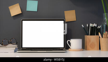 Der Freelancer Arbeitsplatz mit offenen leerer Bildschirm Laptop mit dunklem Hintergrund Wand- und Bürobedarf Stockfoto