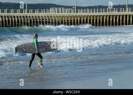 Durban, KwaZulu-Natal, Südafrika, single blond erwachsenen weiblichen Surfer mit Surfbrett zu Fuß aus Meer, Strand, Stadt, Surfen, Lifestyle Stockfoto