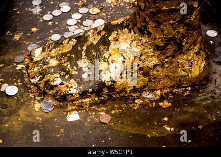 Golden Leaf aufgezeichnet und Thai Badewanne Münze auf den Fuß Buddha Statue Stockfoto