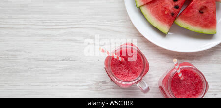 Glas Gläser gefüllt mit Wassermelone Smoothie. Scheiben Wassermelone auf einem weißen Teller. Weiß Holz- Hintergrund. Ansicht von oben, oben, oben. Platz für Text Stockfoto