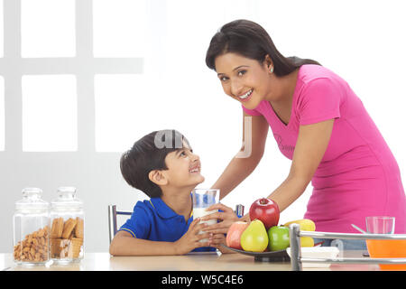 Frau, die ihrem Sohn am Frühstückstisch Milch gab Stockfoto