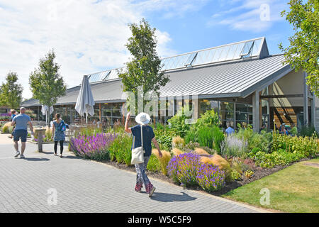 RHS Hyde Hall Garden Centre Menschen zu Fuß vom Parkplatz zu modernen Cafe & Shop Gebäude Eingang Royal Horticultural Society Gärten Essex England Großbritannien Stockfoto