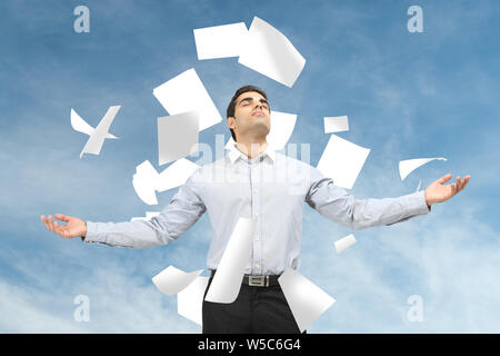 Papiere, die auf einen Geschäftsmann fallen, der mit ausgestreckten Armen steht Stockfoto