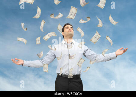 Geld fällt auf einen Geschäftsmann, der mit ausgestreckten Armen steht Stockfoto