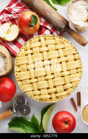 Die Apfelkuchen mit Gitter oben. Raw ungebackene Apfelkuchen mit Werkzeuge und Zutaten zum Kochen. Stockfoto