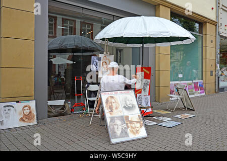 Heidelberg, Deutschland - Juli 2019: Street Artists sittin unter dem großen Sonnenschirm und Portraits von Menschen auf der Straße von Heidelberg Stockfoto