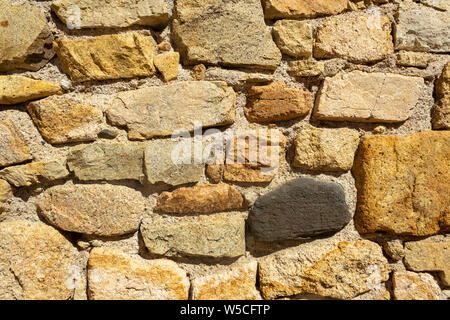 Detail einer Steinmauer aus unregelmäßig geformten und gefärbten Stein, bei starker Sonneneinstrahlung. Geeignet als Hintergrundbild Stockfoto
