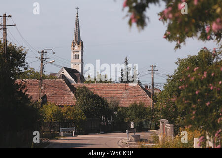 Ländliche Szene aus einem Dorf in Rumänien: Straße, Häuser und eine Kirche Turm im Hintergrund Stockfoto