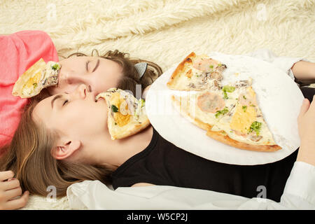 Überessen Mädchen Lügen mit Pizza Stücke im Mund Stockfoto