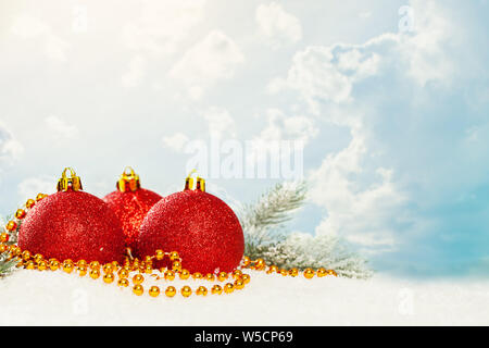 Christbaumkugeln, gold Garland und Grüne Tanne Zweig auf weißem Schnee gegen den blauen Himmel mit weißen Wolken. Winterurlaub Hintergrund Stockfoto