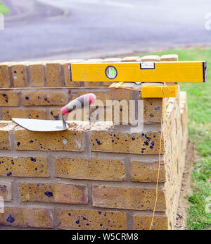 Maurer Kelle, Wasserwaage, block-Zeile und Prickeln auf einer teilweise gebaut Ziegelfabrik container. Stockfoto